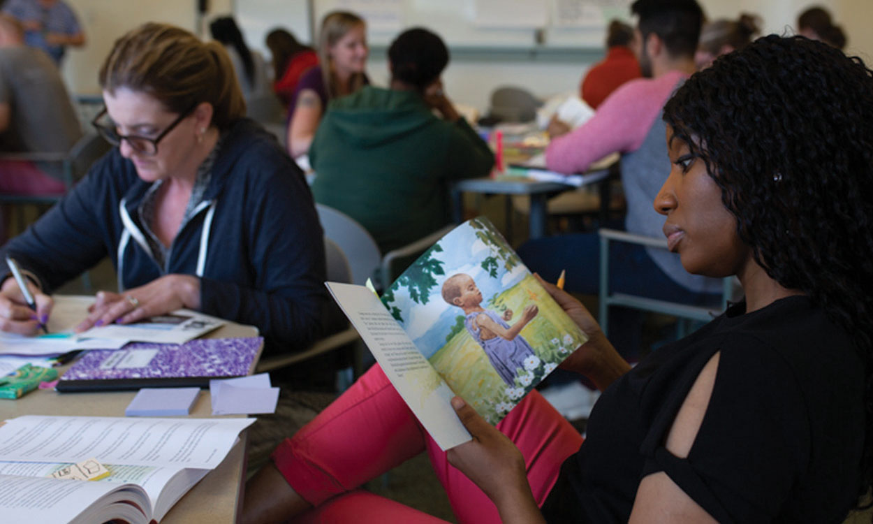 Educator sitting a table, looking through a children's book.