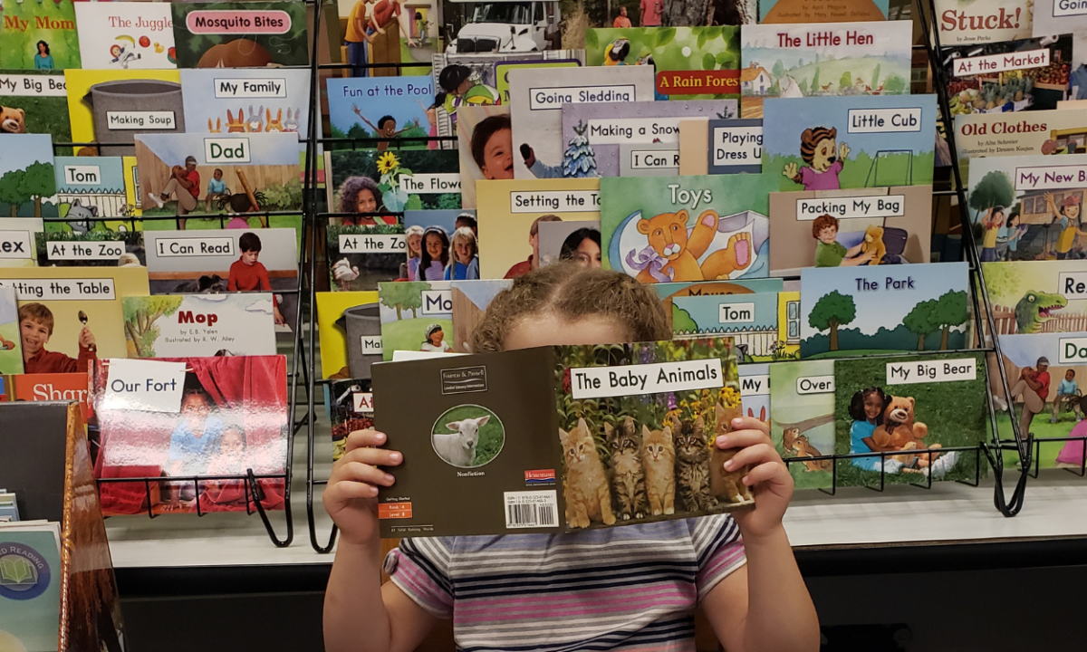 Child reading a book with leveled texts in the background.